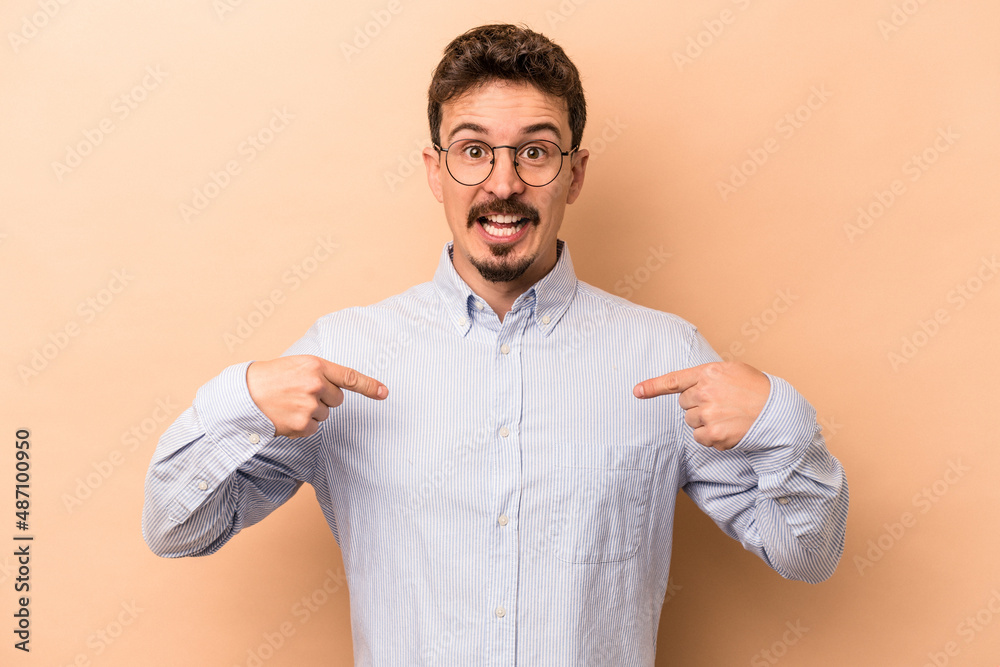 Young caucasian man isolated on beige background surprised pointing with finger, smiling broadly. Young caucasian man isolated on beige background surprised pointing with finger, smiling broadly.