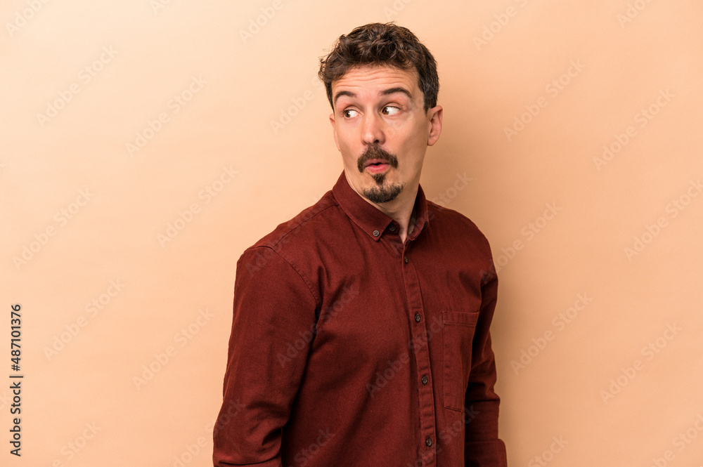 Young caucasian man isolated on beige background looks aside smiling, cheerful and pleasant. Young caucasian man isolated on beige background looks aside smiling, cheerful and pleasant.
