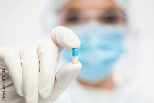 Female UK pharmacist wearing PPE personal protective equipment holding antibiotic pill