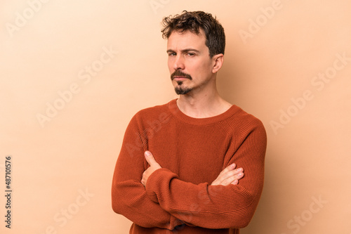 Young caucasian man isolated on beige background suspicious, uncertain, examining you.