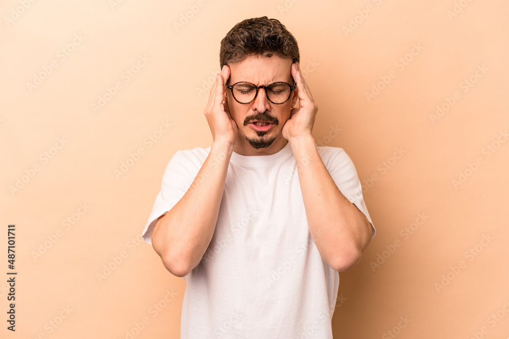 Young caucasian man isolated on beige background having a head ache, touching front of the face. Young caucasian man isolated on beige background having a head ache, touching front of the face.
