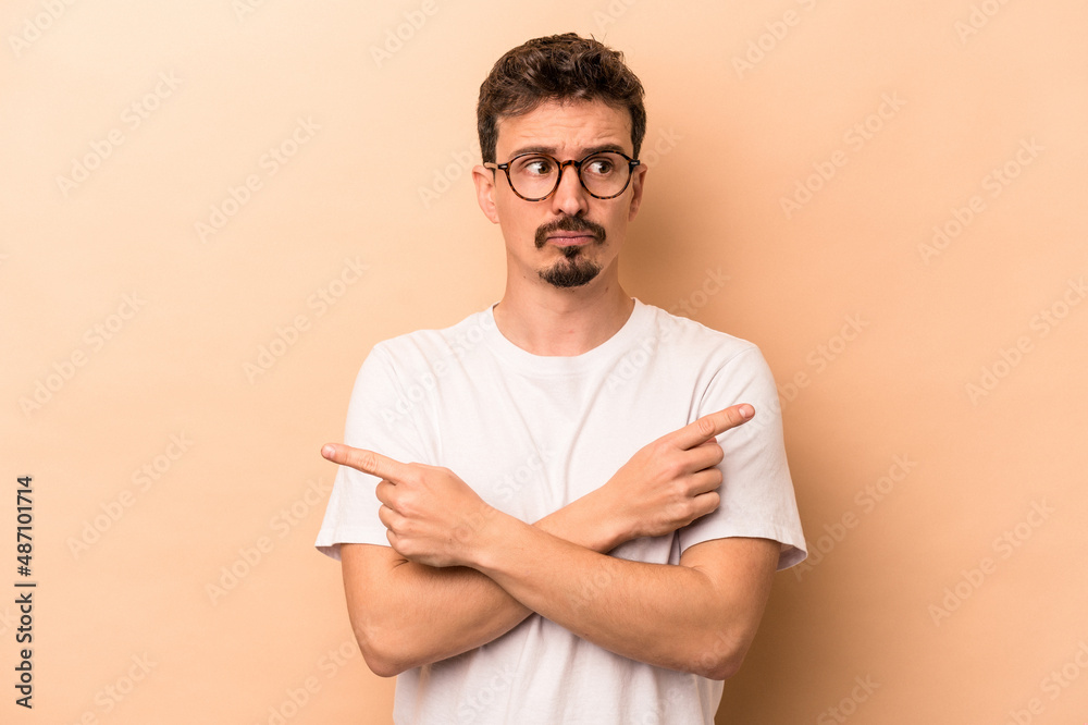 Young caucasian man isolated on beige background points sideways, is trying to choose between two options. Young caucasian man isolated on beige background points sideways, is trying to choose between two options.