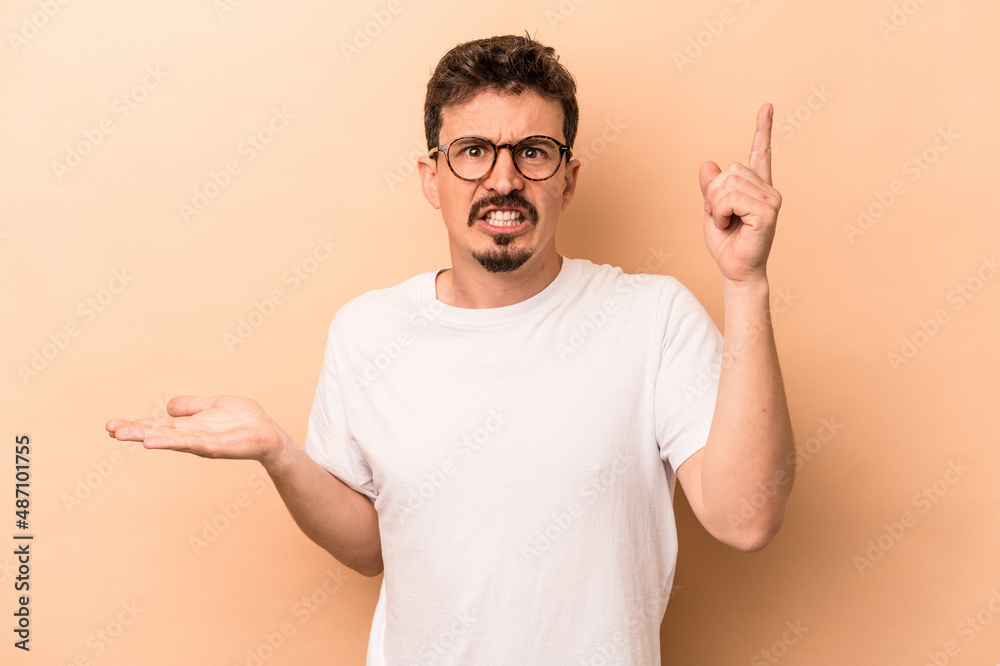 Young caucasian man isolated on beige background holding and showing a product on hand. Young caucasian man isolated on beige background holding and showing a product on hand.