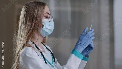 Woman doctor wearing a face mask and medical gown preparing holding syringe for injection covid19 vaccination. Female nurse with liquid medicine antibiotic flu antivirus vaccine protection from virus photo