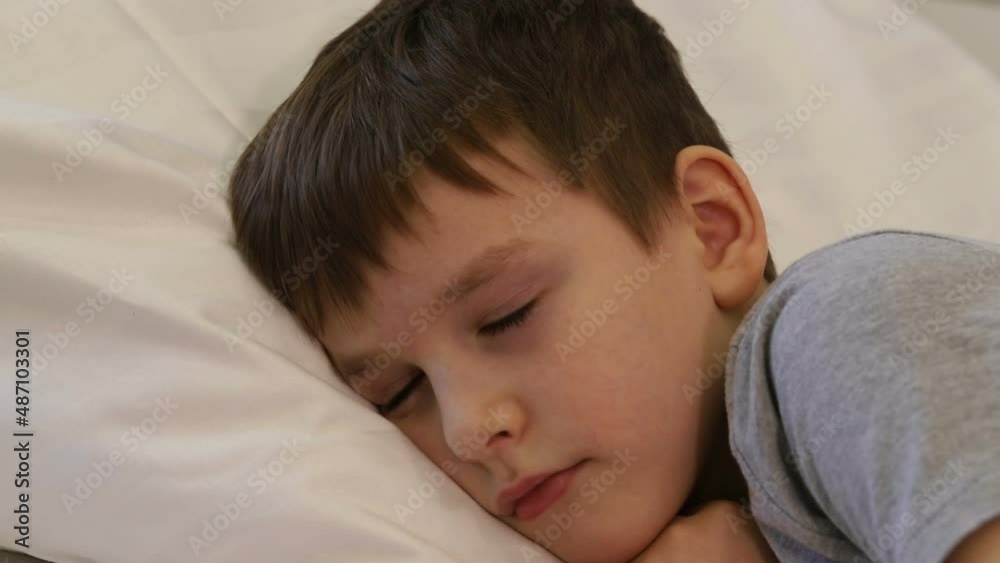 A seven-year-old boy falls asleep passionately on his bed on a pillow.