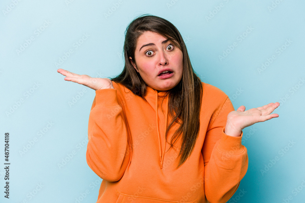 Young caucasian overweight woman isolated on blue background confused and doubtful shrugging shoulders to hold a copy space.