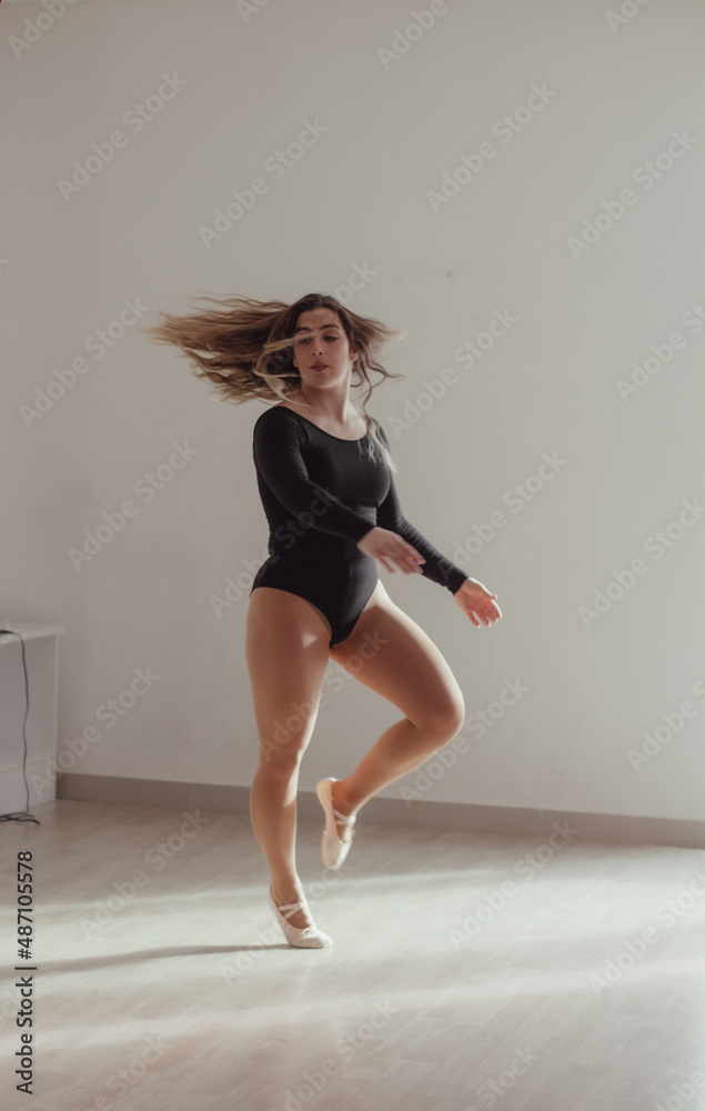 A woman jumping into a dance pose in a dance studio, in front of a window, dressed in a dance outfit. A woman jumping into a dance pose in a dance studio, in front of a window, dressed in a dance outfit.