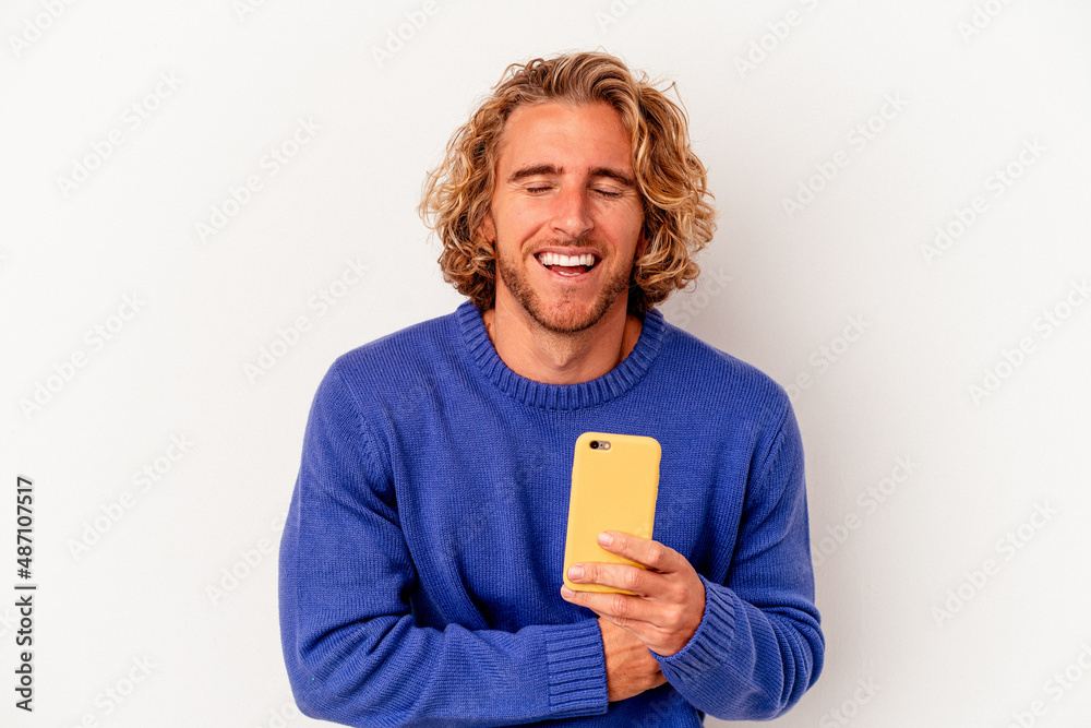 Young caucasian man holding mobile phone isolated on white background laughing and having fun. Young caucasian man holding mobile phone isolated on white background laughing and having fun.
