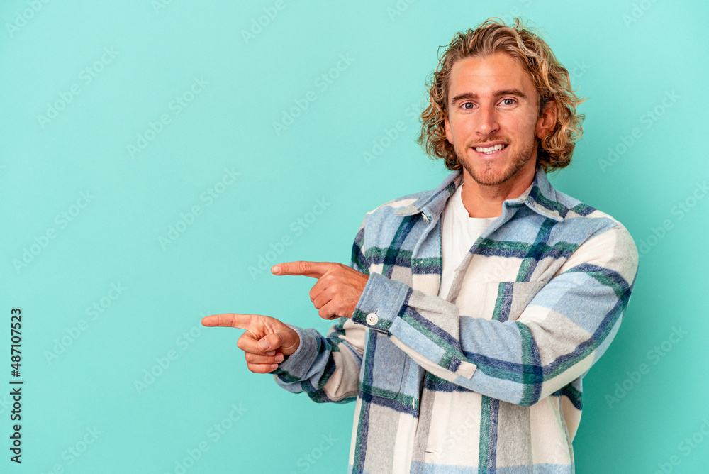 Young caucasian man isolated on blue background excited pointing with forefingers away.