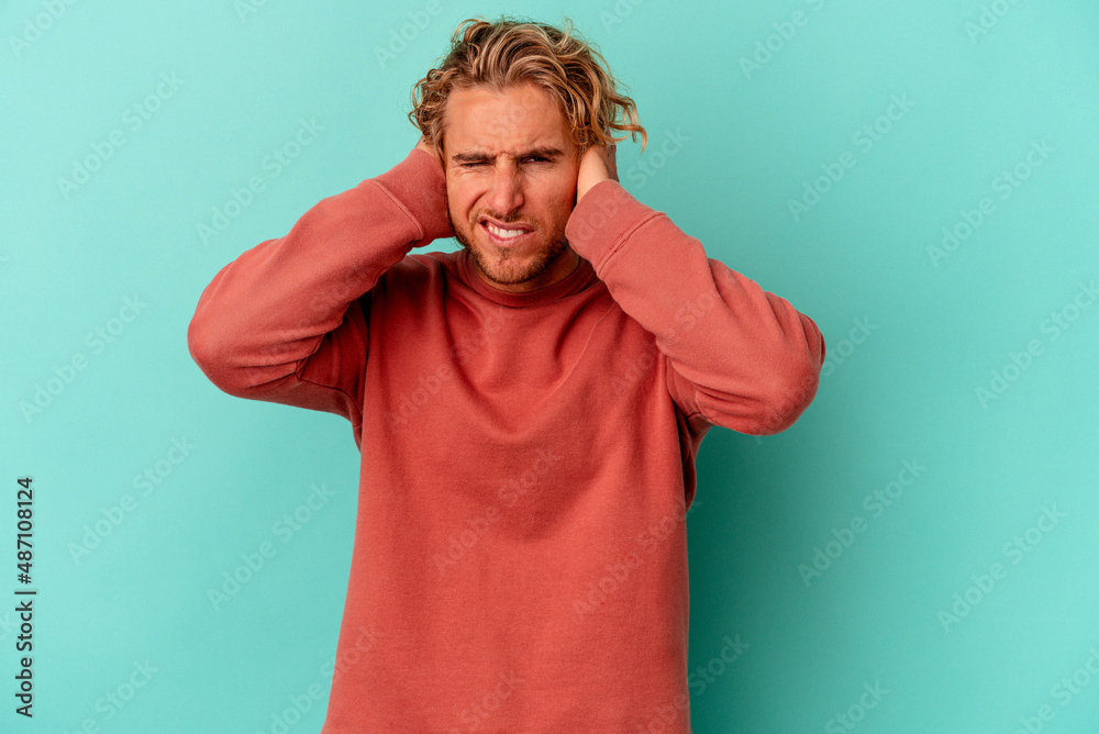 Young caucasian man isolated on blue background covering ears with hands. Young caucasian man isolated on blue background covering ears with hands.