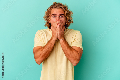 Young caucasian man isolated on blue background shocked, covering mouth with hands, anxious to discover something new.