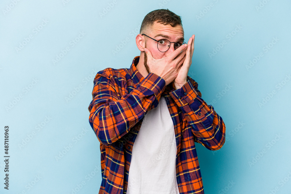 Young caucasian man isolated on blue background blink through fingers frightened and nervous. Young caucasian man isolated on blue background blink through fingers frightened and nervous.