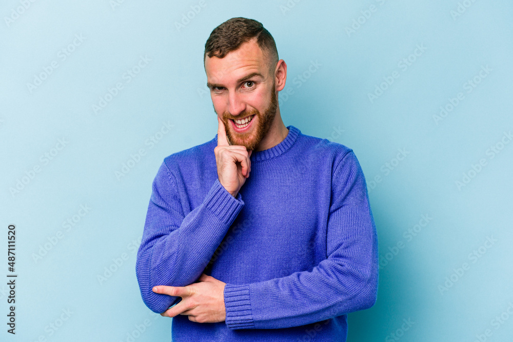 Young caucasian man isolated on blue background smiling happy and confident, touching chin with hand. Young caucasian man isolated on blue background smiling happy and confident, touching chin with hand.