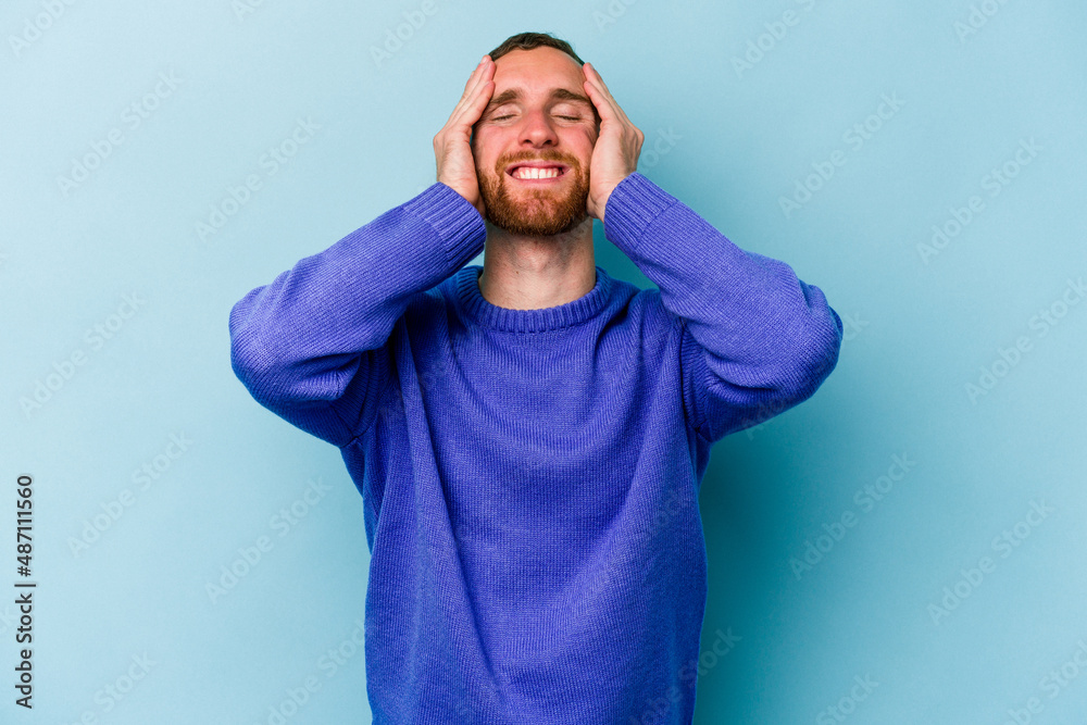 Young caucasian man isolated on blue background laughs joyfully keeping hands on head. Happiness concept. Young caucasian man isolated on blue background laughs joyfully keeping hands on head. Happiness concept.