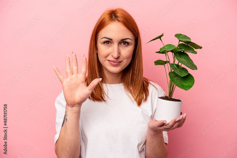 Young caucasian woman holding a plant isolated on pink background Young caucasian woman holding a plant isolated on pink background smiling cheerful showing number five with fingers. Young caucasian woman holding a plant isolated on pink background Young caucasian woman holding a plant isolated on pink background smiling cheerful showing number five with fingers.