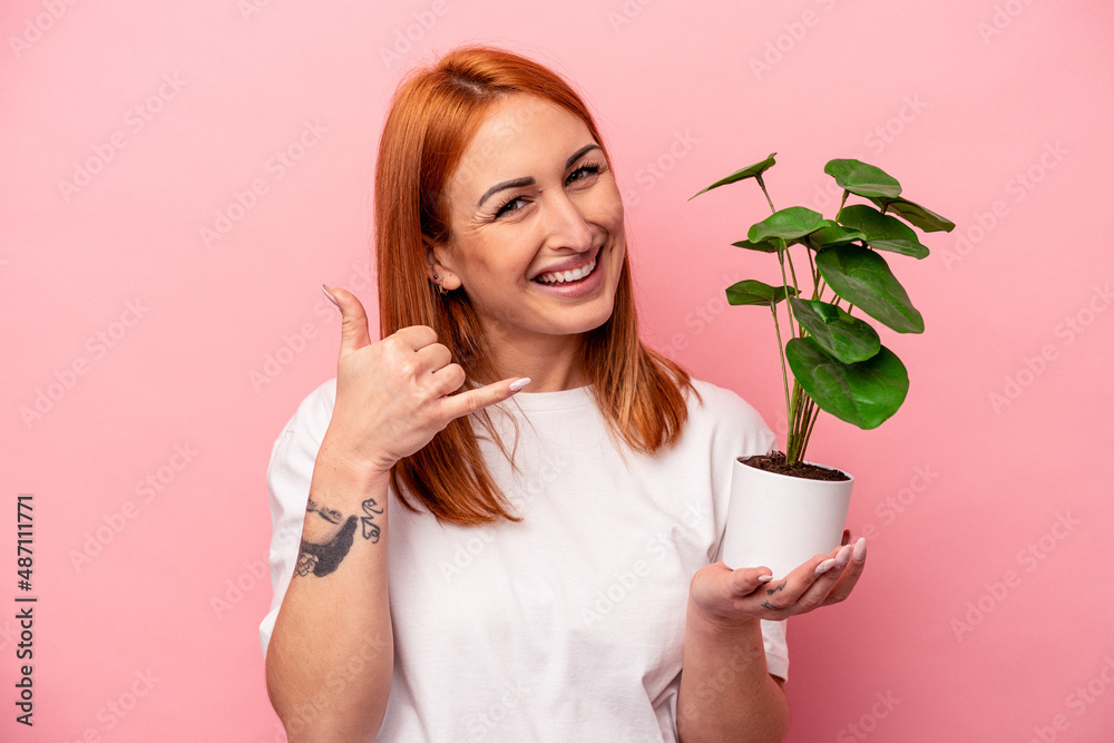 Young caucasian woman holding a plant isolated on pink background Young caucasian woman holding a plant isolated on pink background showing a mobile phone call gesture with fingers. Young caucasian woman holding a plant isolated on pink background Young caucasian woman holding a plant isolated on pink background showing a mobile phone call gesture with fingers.