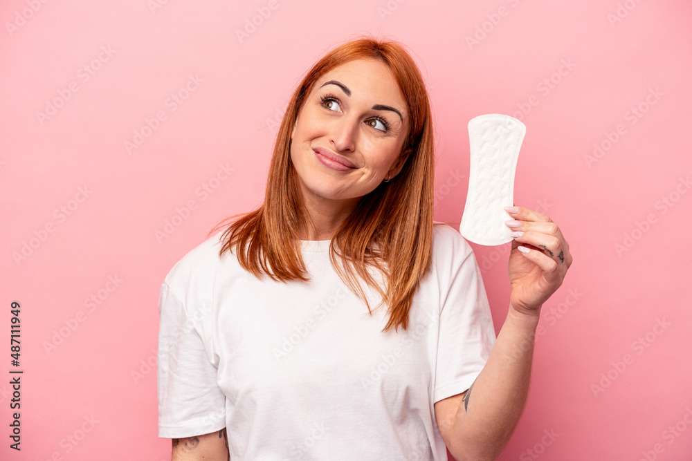 Young caucasian woman holding sanitary napkin isolated on pink background dreaming of achieving goals and purposes Young caucasian woman holding sanitary napkin isolated on pink background dreaming of achieving goals and purposes