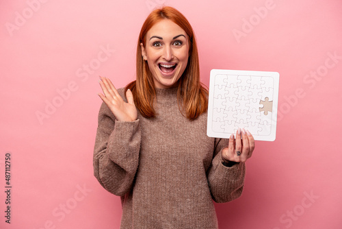 Young caucasian woman holding puzzle isolated on pink background surprised and shocked.