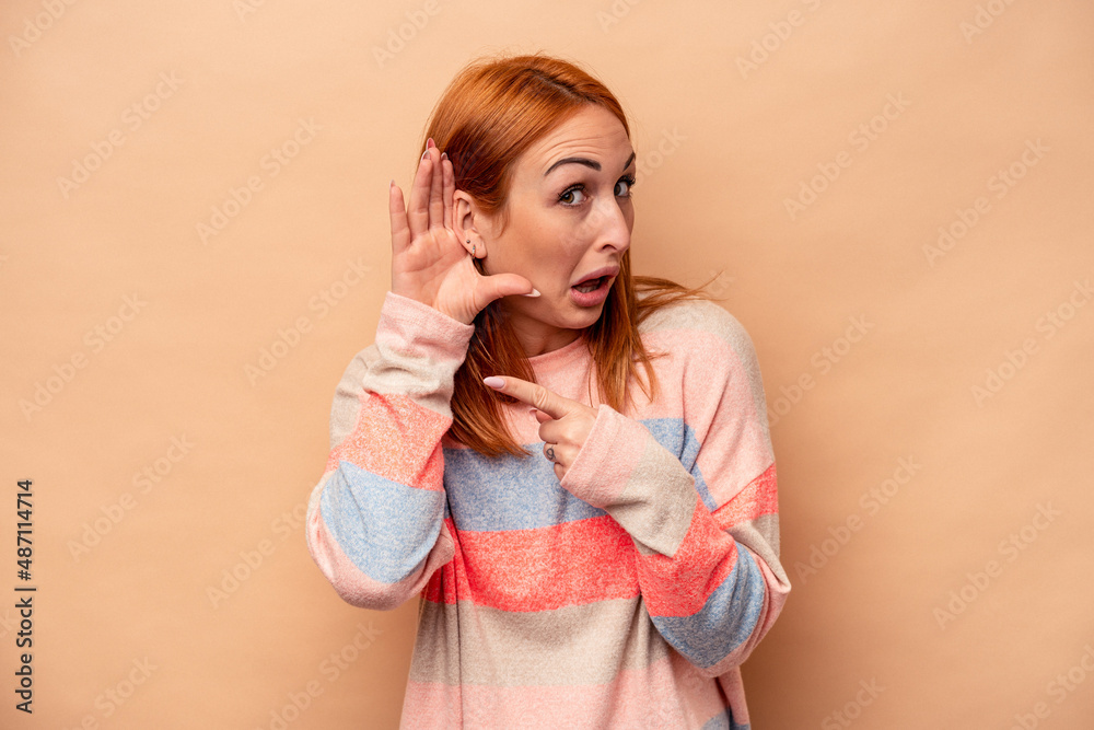 Young caucasian woman isolated on beige background trying to listening a gossip. Young caucasian woman isolated on beige background trying to listening a gossip.