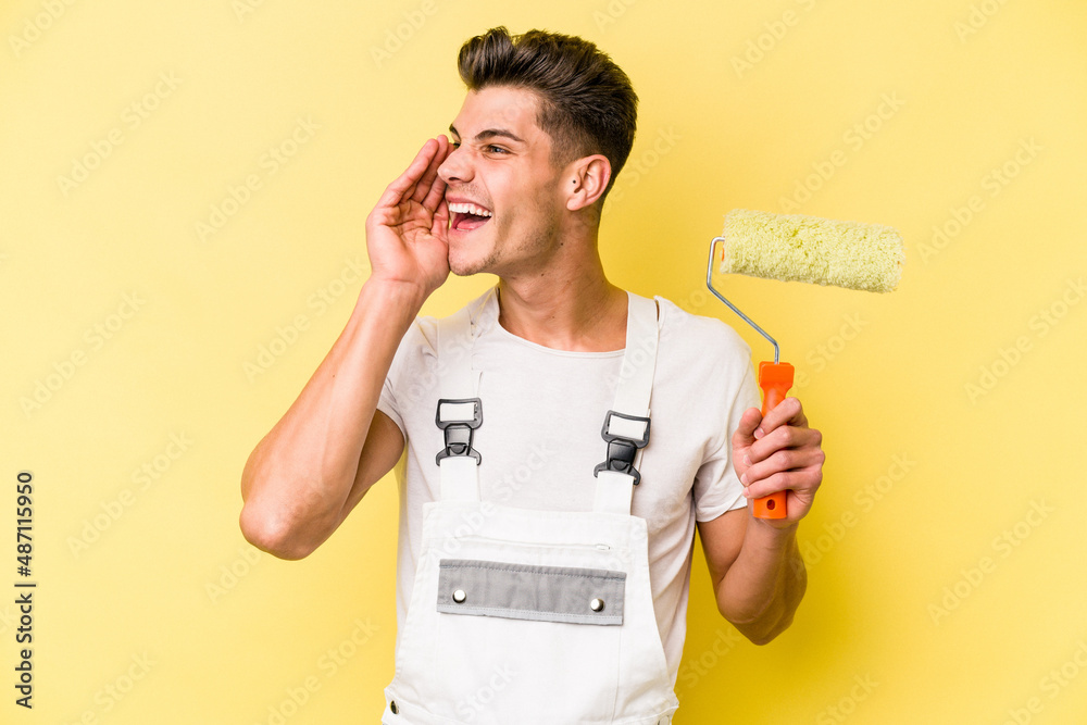 Young painter man isolated on yellow background shouting and holding palm near opened mouth.