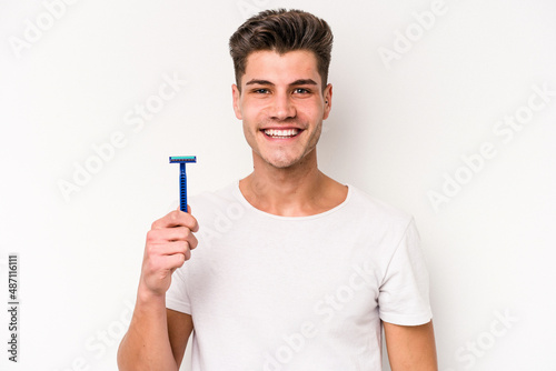 Young caucasian man shaving his beard isolated on white background happy, smiling and cheerful.