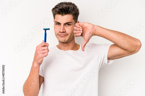 Young caucasian man shaving his beard isolated on white background showing a dislike gesture, thumbs down. Disagreement concept.