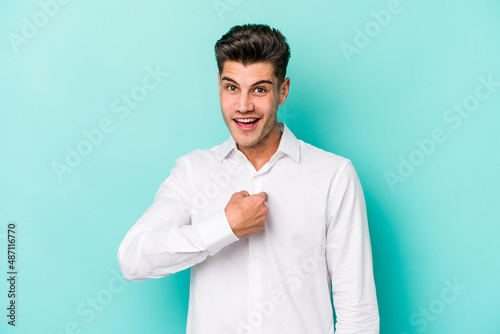 Young caucasian man isolated on blue background surprised pointing with finger, smiling broadly.