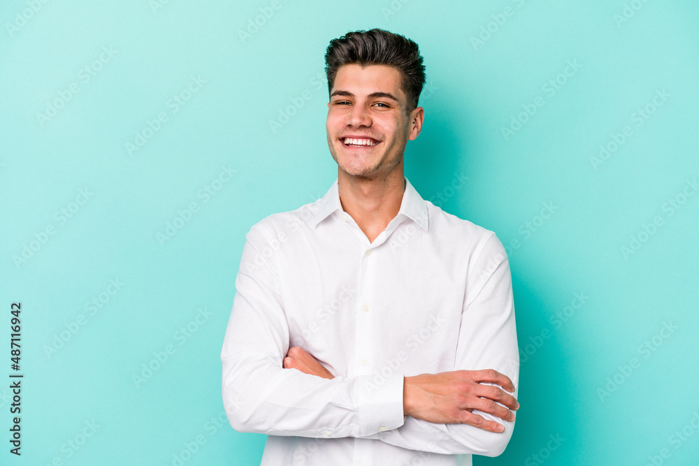 Young caucasian man isolated on blue background who feels confident, crossing arms with determination. Young caucasian man isolated on blue background who feels confident, crossing arms with determination.
