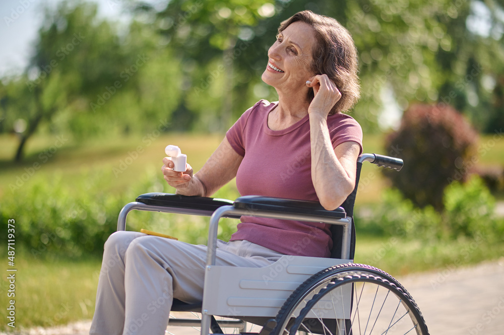 A smiling woman on a wheel-chair putting on wireless headphones A smiling woman on a wheel-chair putting on wireless headphones