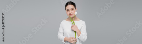 Photographie Woman with down syndrome holding white tulip and looking at camera isolated on g