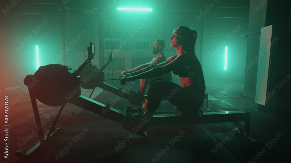 Slow motion: Man and woman training on a rowing machine in gym