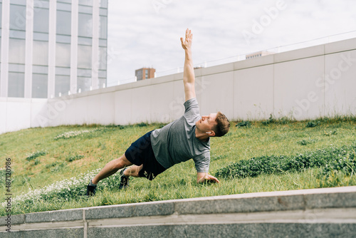 Young man has fitness workout. Male athlete does abs exercise, sport and training outdoor and stands in plank. People sport and healthy lifestyle concept.