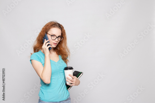 a girl in a blue T-shirt with a phone and coffee on a light background