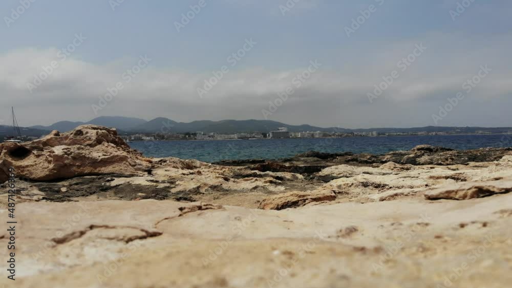 Scenic close up view of Ibiza, Sant Antoni rocky limestone beach on a warm sunny day with balearic sea an mountains in the background in Spain Scenic close up view of Ibiza, Sant Antoni rocky limestone beach on a warm sunny day with balearic sea an mountains in the background in Spain