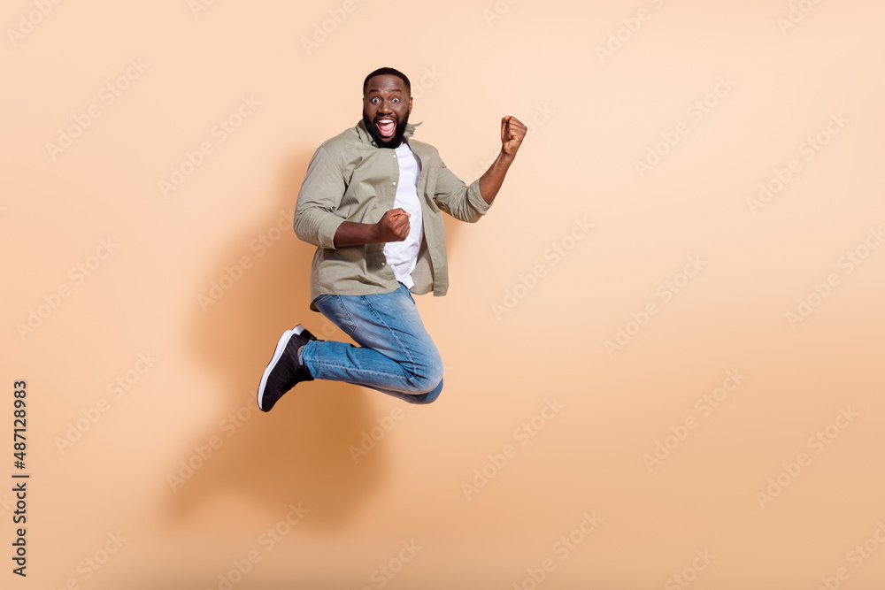 Full size impressed millennial brunet guy jump yell wear shirt jeans shoes isolated on beige background