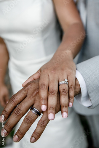 Newlywed couple Bride and African American groom in grey suit showing their wedding rings on hands Black wedding ring and white diamond ring Just married young couple showing up their rings 