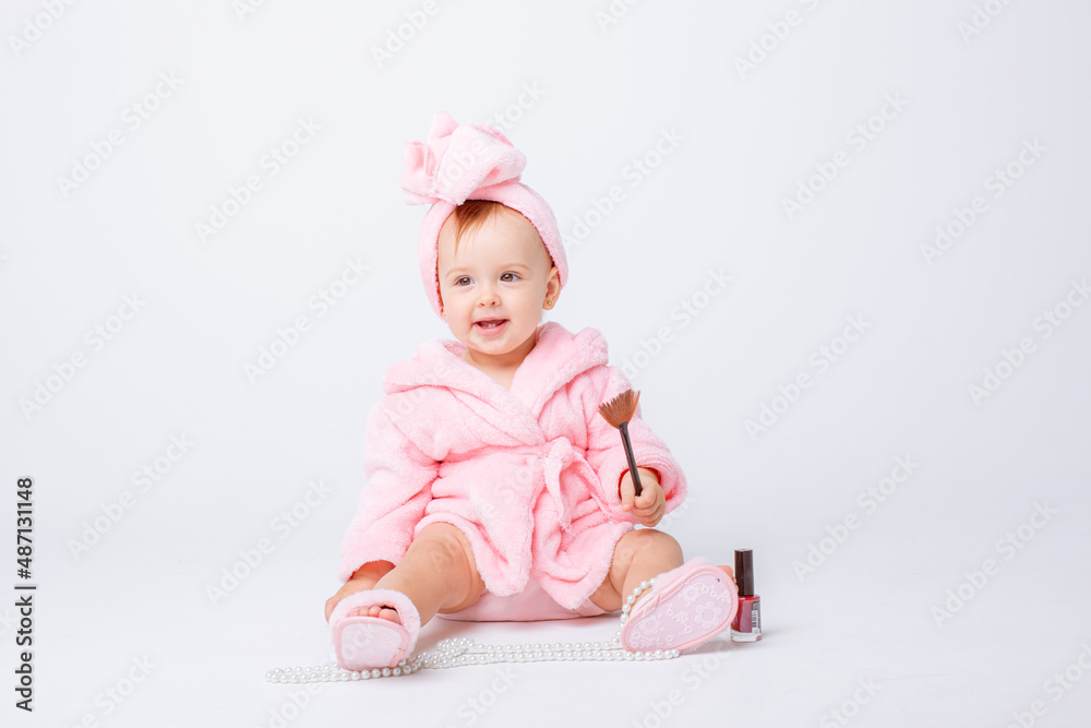Cute little baby girl in pink terry with makeup isolated on a white background, repeats the behavior of mom Cute little baby girl in pink terry with makeup isolated on a white background, repeats the behavior of mom