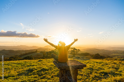 Teenager sitting on a wall enjoying a beautiful sunset with his hands raised. 
