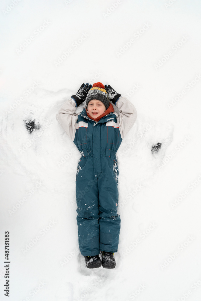 Happy child boy playing on winter in the snow. Kid making snow angel. Top view. Vertical frame.