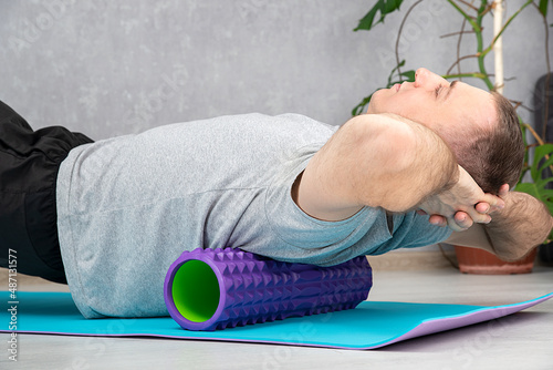 Man doing myofascial release of hyper-flexible muscles of back with massage foam roller. Self-massage of the back. photo