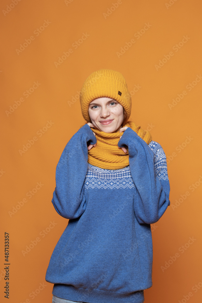 young red-haired girl in a warm hat and a knitted sweater on a yellow background