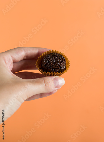 A woman's hand holding a vegan brigadeiro. Typical Brazilian sweet. Orange background