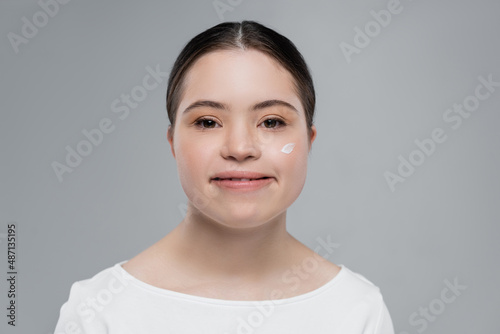 Smiling woman with down syndrome and cream on face isolated on grey