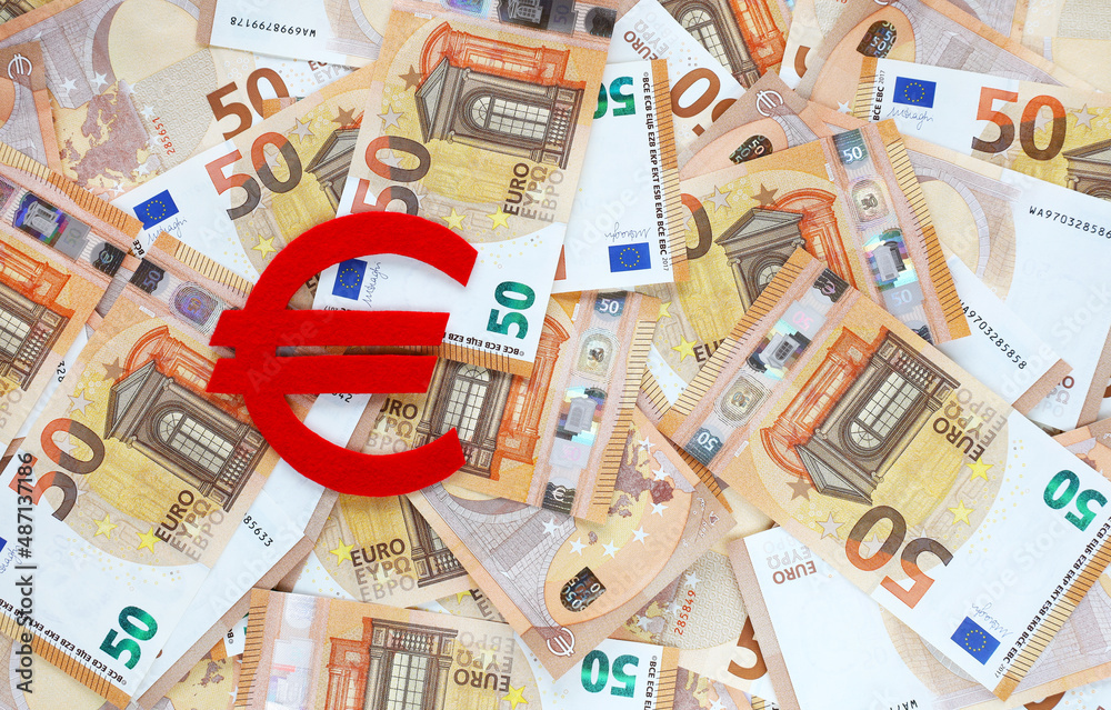 Euro currency symbol cut out of red felt on background covered with 50 euro banknotes. Financial, bank, money, economy, business concept. Place for text.