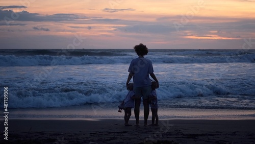 Lovely family vacation, silhouette of single mother with two toddlers running from huge ocean waves on the sunset 