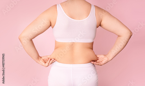 A young woman pinches fat on the side of her waist to show a flabby, overweight body after pregnancy and childbirth.