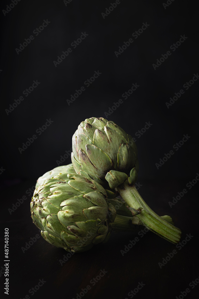 Fototapeta premium Fresh and raw artichokes on a dark background with space for text