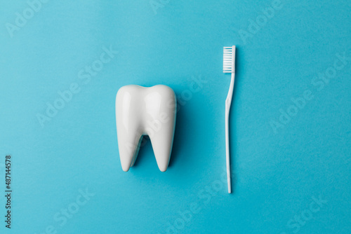 The concept of dental health and dental care. Dentist's day. A white toothbrush lies next to a white tooth on a blue background. A healthy tooth. Space for text. Close-up