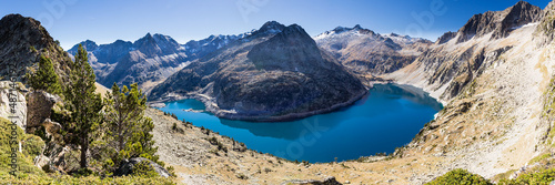 Large panorama d'un lac de montagne en forme d'arc photographié d'un point haut avec ciel bleu. Lac de Cap de Long, Hautes Pyrénées, réserve du Néouvielle.