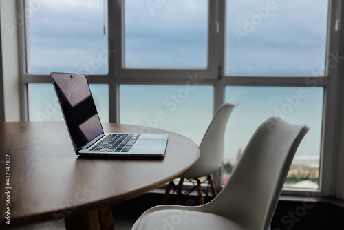 workplace, laptop on a wooden table by the window overlooking the sea.